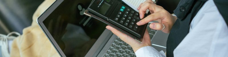 Close-up of a person using a calculator with a laptop, symbolizing home office productivity.